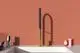 Küchenarmatur mit einem hohen, geschwungenen Auslauf und gebürstetem Gold-Finish. Ideal Standard, modern installiert über einem weißen Waschbecken in einem minimalistischen Raum.